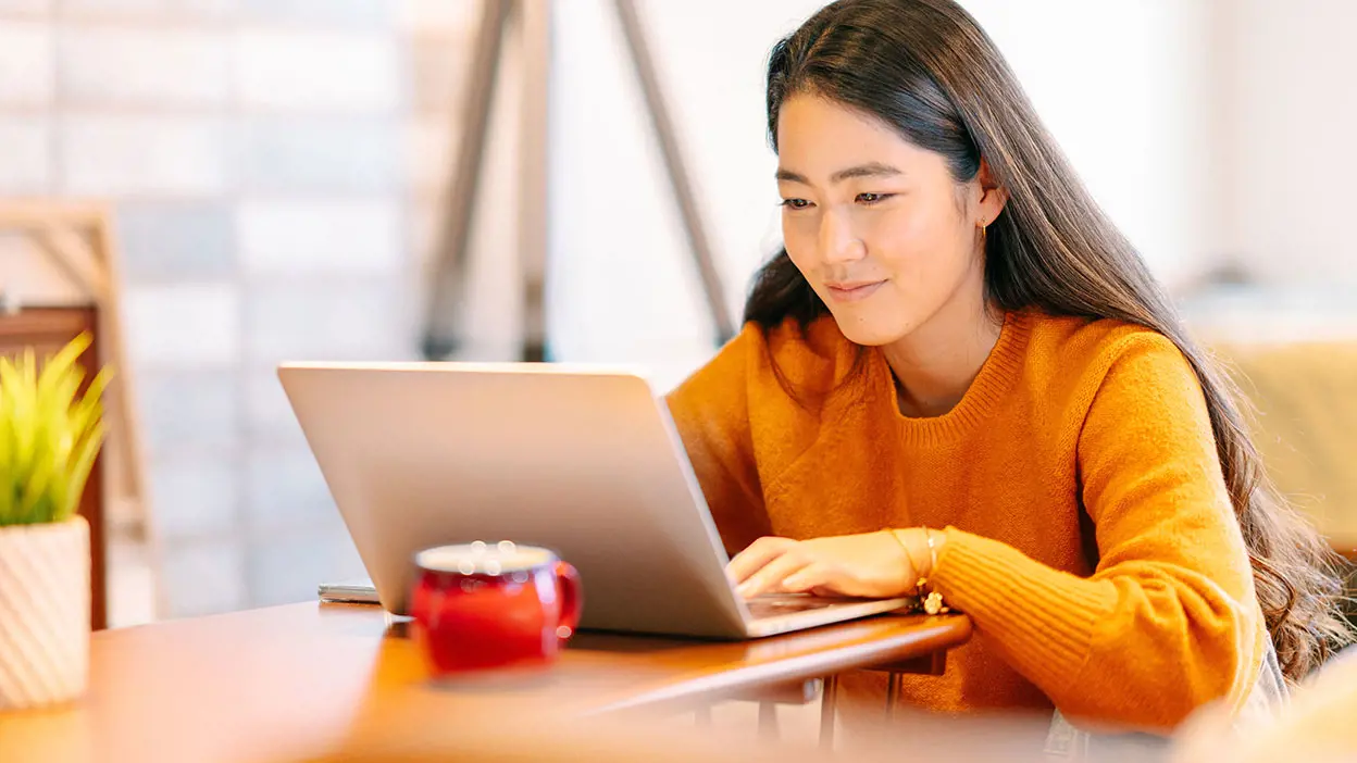 Woman in orange sweater sitting in front of a laptop at a desk