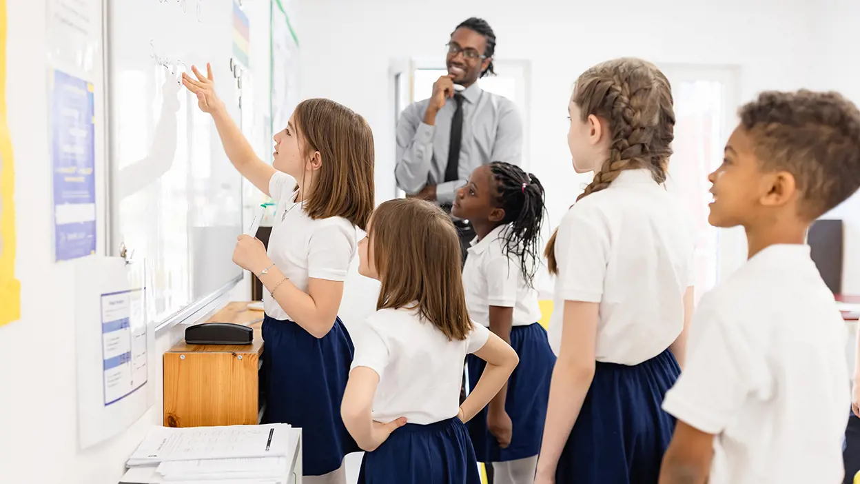 Children in white and blue uniforms writing on a white board in class