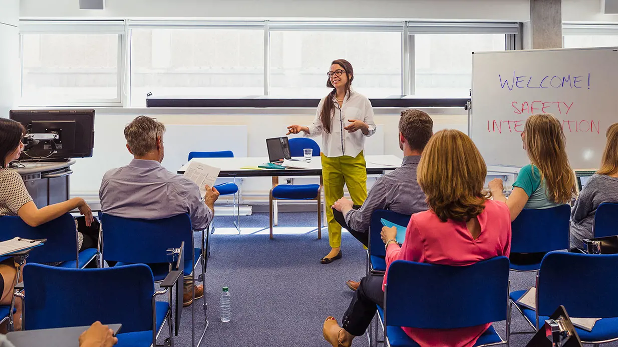 Female programme trainer in front of a flip chart facing people sitting in chairs