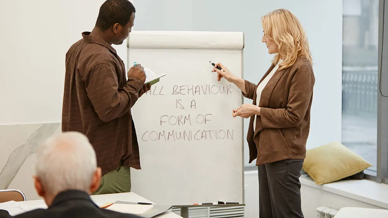 A woman with a marker and a man with a notebook in front of a Verbal Intervention training flip chart
