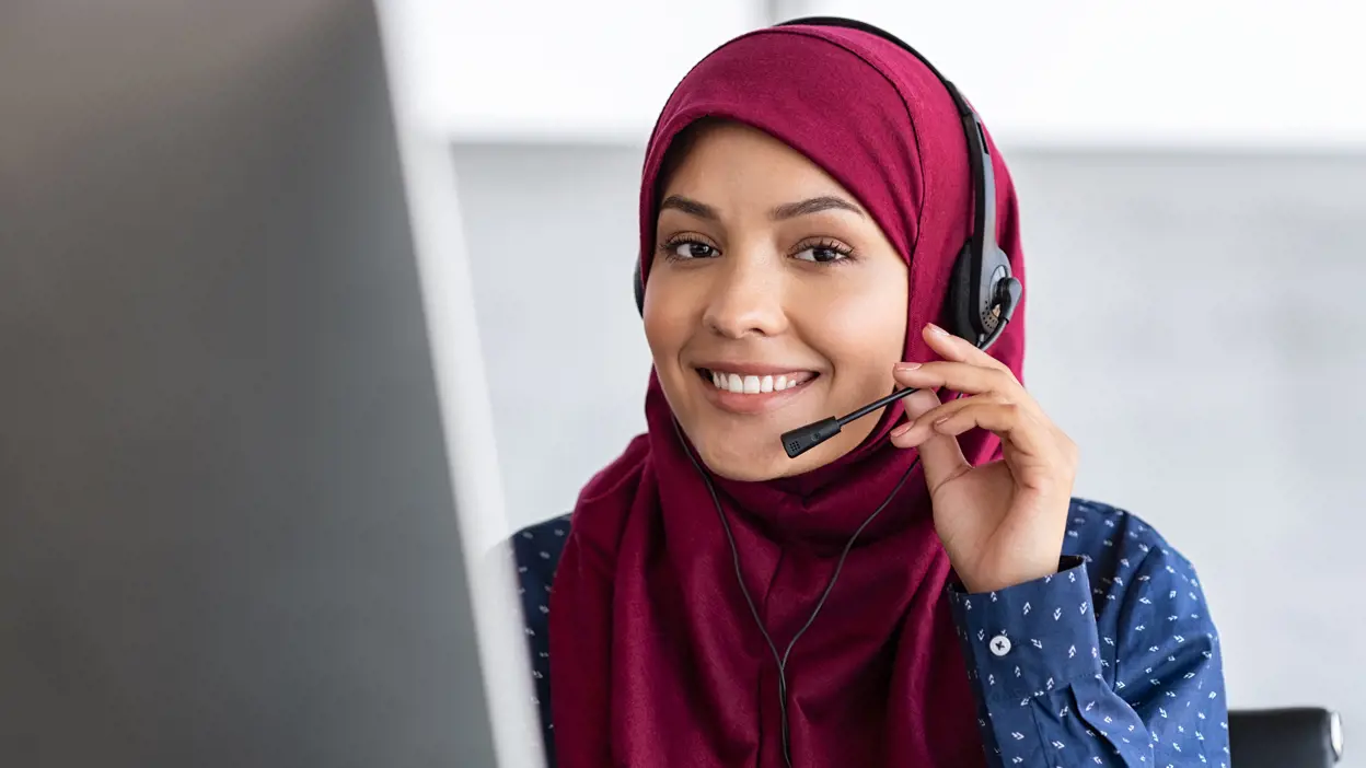 A woman wearing a hijab speaking on a headset.