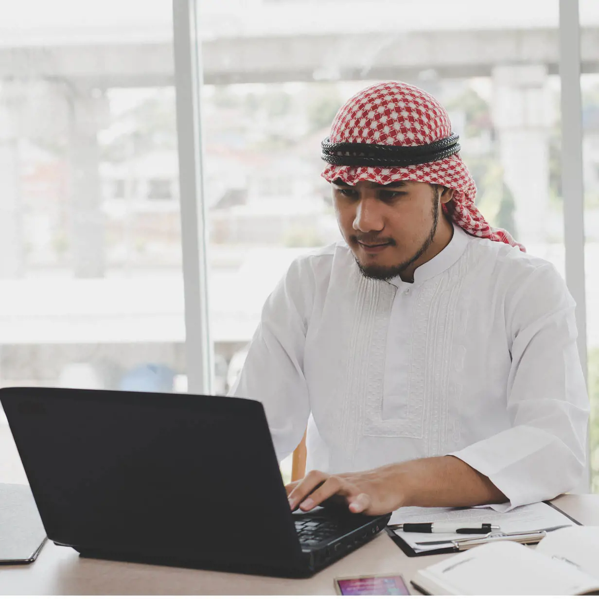 A man wearing a keffiyeh using a laptop. 