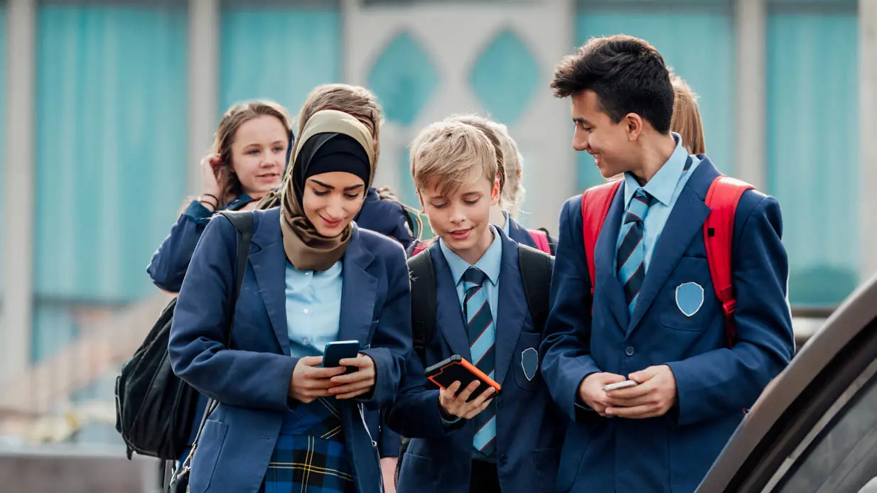A group of happy school children looking at phones.