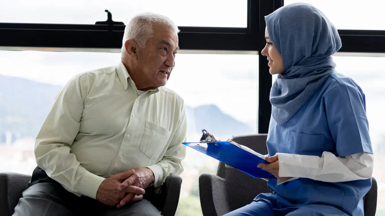 A medical professional in a hijab talking with an elderly patient. 