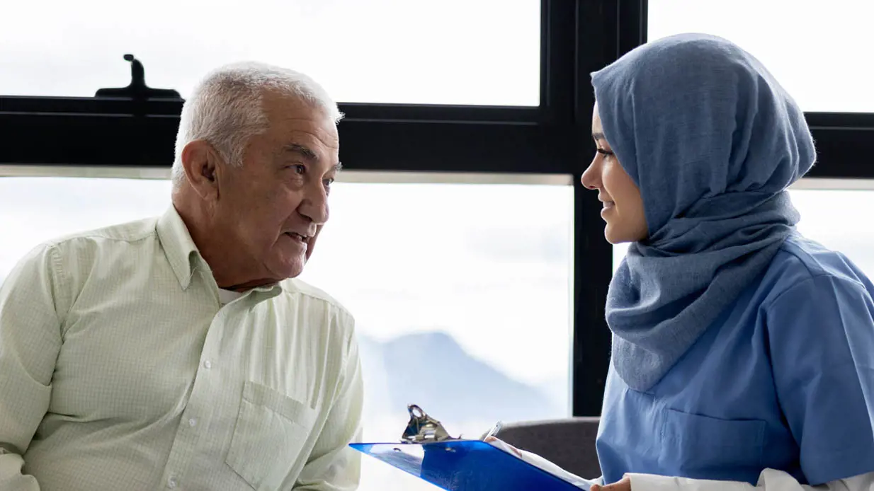 A medical professional in a hijab talking with an elderly patient. 
