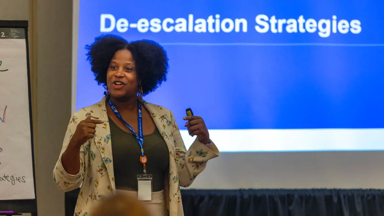 A woman presenting about de-escalation strategies.