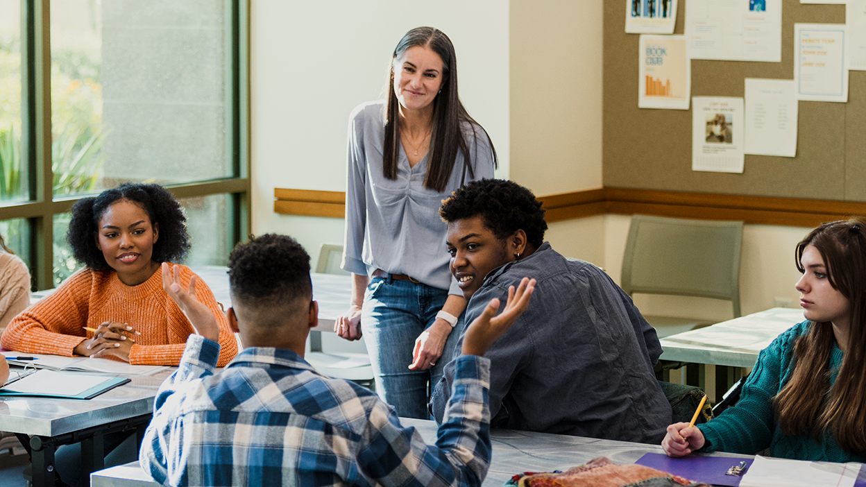 A teacher in a classroom listening to a student.