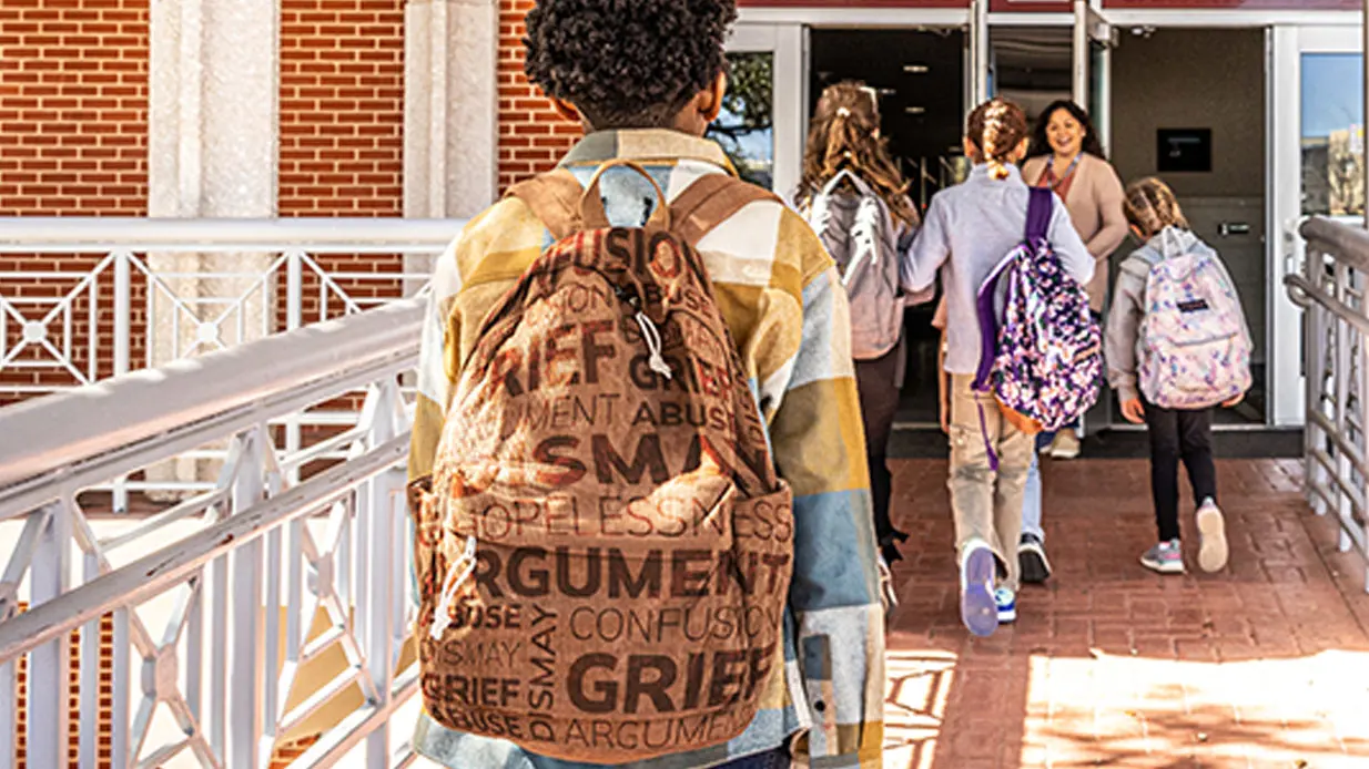 Child walking into school wearing backpack.