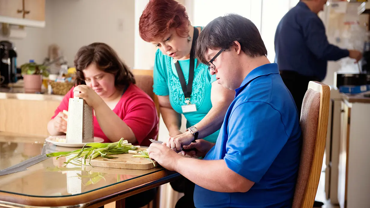 Human Services professional assisting client cutting vegetables.