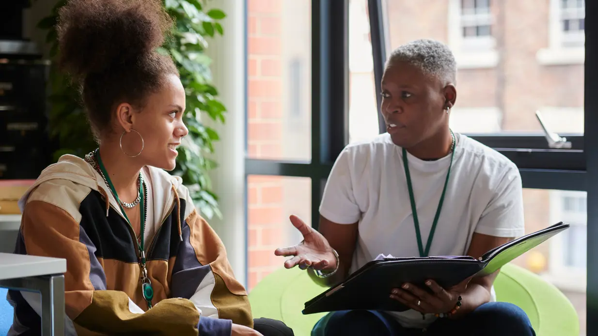 Two women engaged in conversation while seated in a chair, sharing thoughts and laughter in a relaxed setting.