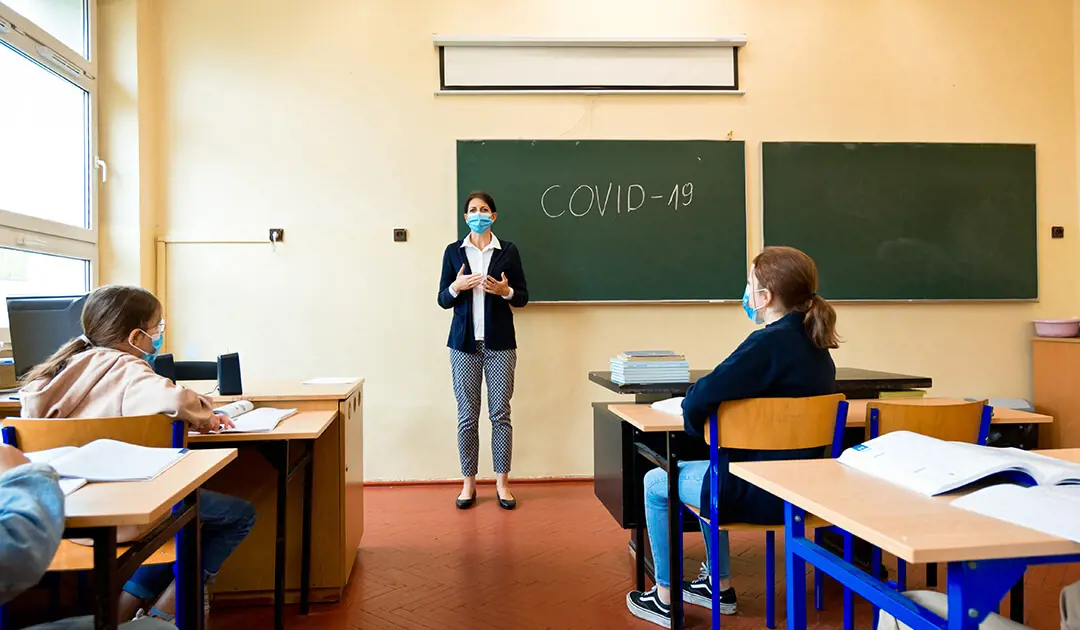Masked teacher at the front of the classroom during covid