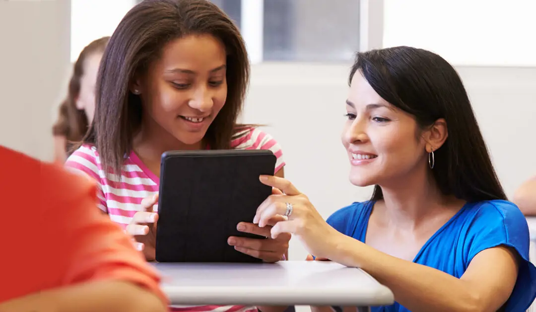 Female teacher helping female student with tablet