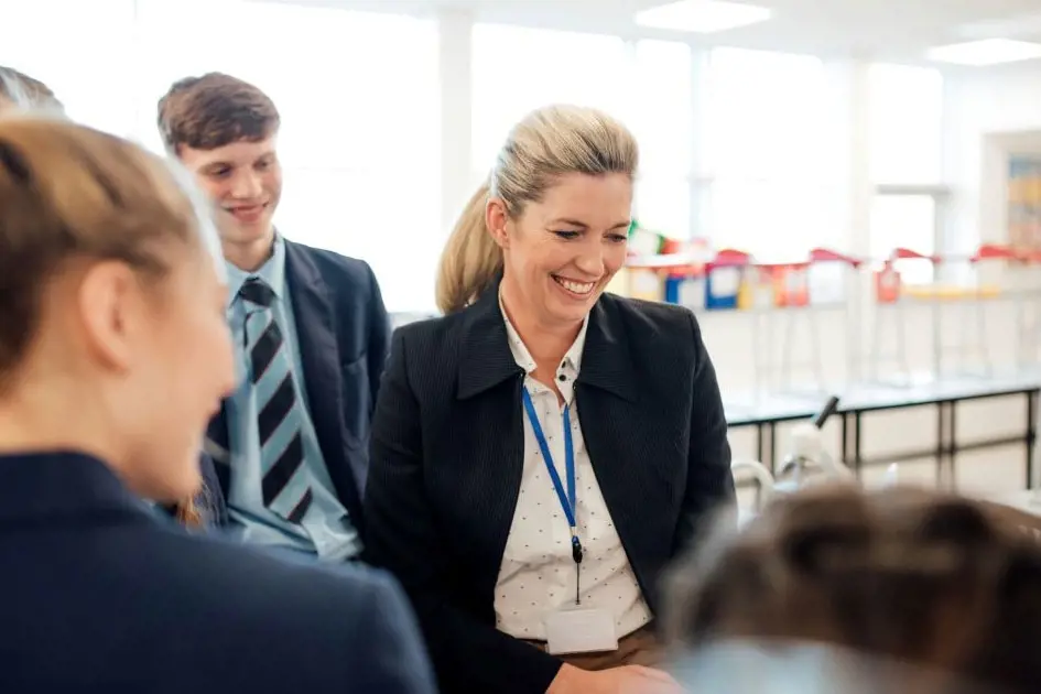 Teacher smiling talking to students within a classroom 