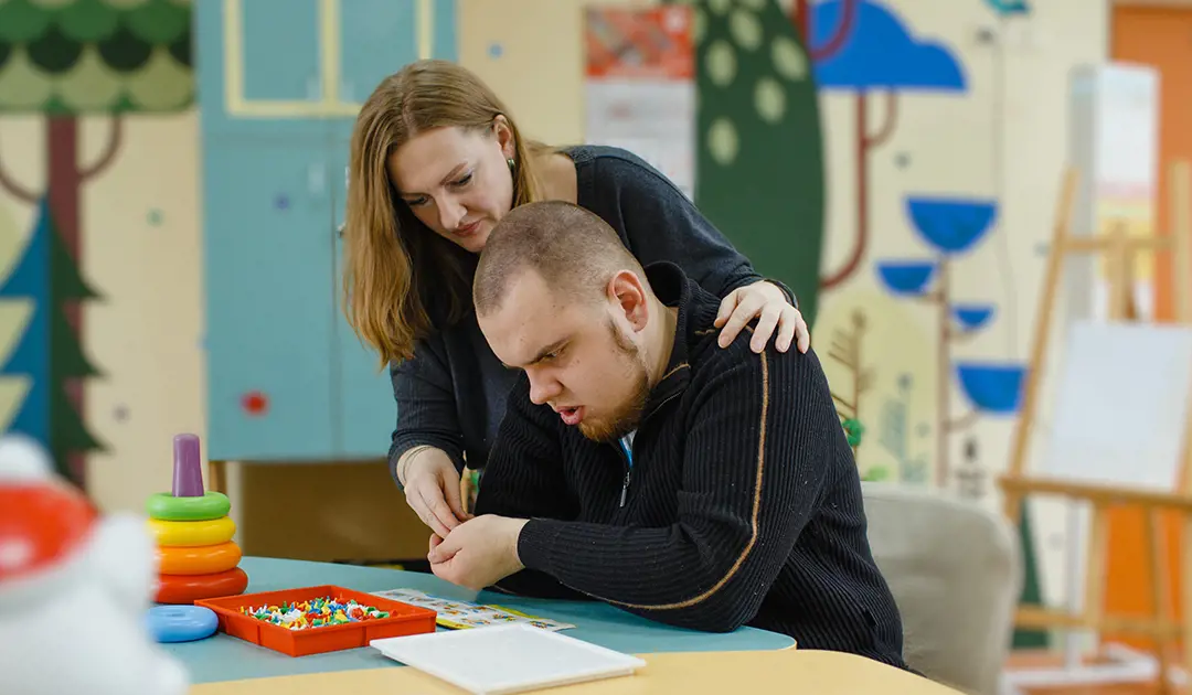 Teacher helping disabled student at a table