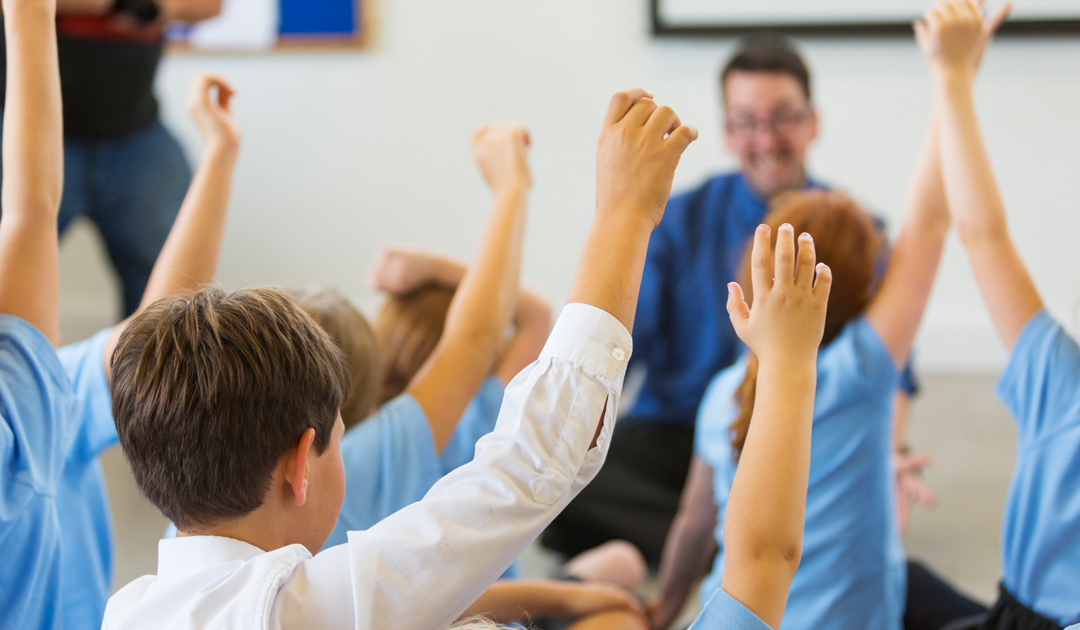Students raising hands in a classroom.